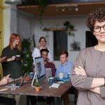 Smiling businesswoman with curly hair stands confidently in a modern office space with colleagues.